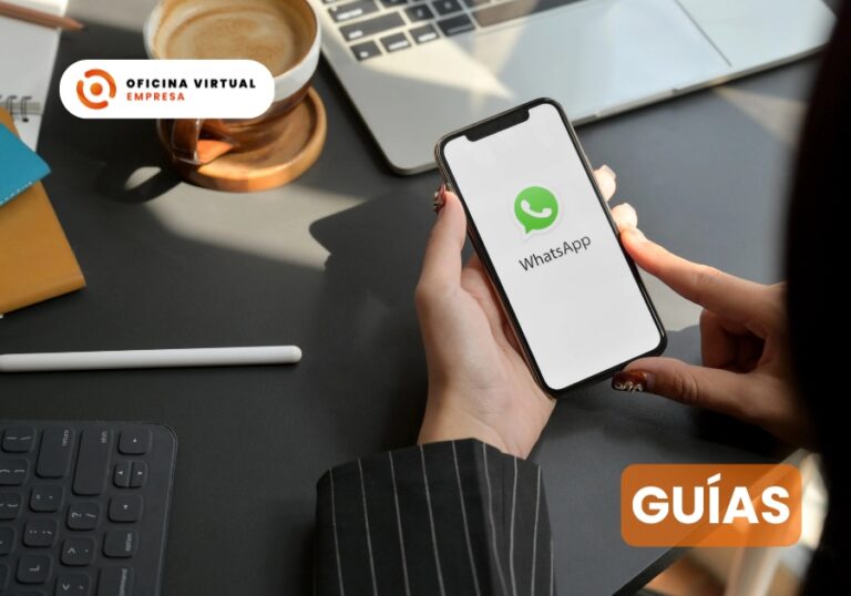 Persona con un móvil abriendo WhatsApp sobre un escritorio